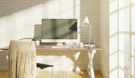 Front view of creative designer workplace with empty computer screen placed on desk with coffee cup, supplies and other items. Brick wall background. Mock up, 3D Rendering